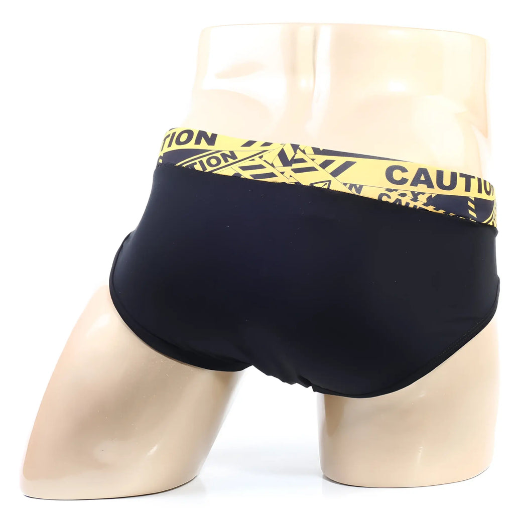 Black swim trunks by Metromalewear with bold yellow caution tape patterned waistband for a striking look