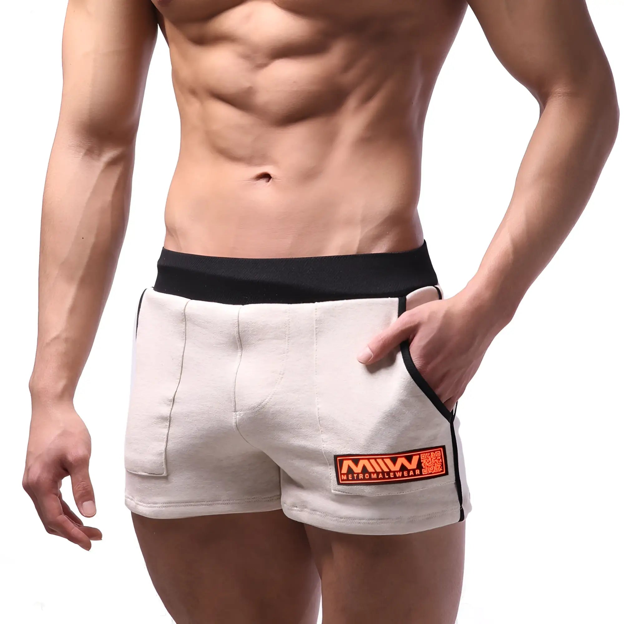 Beige cotton athletic shorts with black elastic waistband and orange logo patch on lower right leg by metromalewear