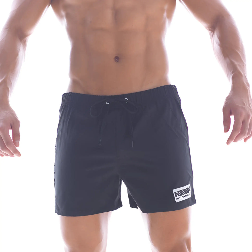 Black athletic MetroMaleWear flexible swim trunks with drawstring waistband and white logo patch on lower right leg