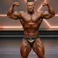 A muscular man wearing metromalewear metro musclewear gold and black bodybuilding competition trunks