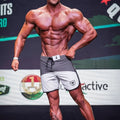 Gray and white metromalewear cordobaphysique board shorts with black drawstring and shield logo on left leg