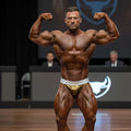 A muscular man posing confidently in gold and white MetroMaleWear MetroMuscleWear Cortina muscle trunk briefs