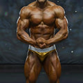 A muscular male bodybuilder wearing shiny gold and silver metromalewear metromusclewear diy competition briefs