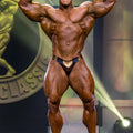 A muscular bodybuilder wearing black and gold textured metallic MetroMaleWear MetroMuscleWear Fortuna competition briefs