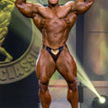 A muscular bodybuilder wearing black and gold textured metallic MetroMaleWear MetroMuscleWear Fortuna competition briefs