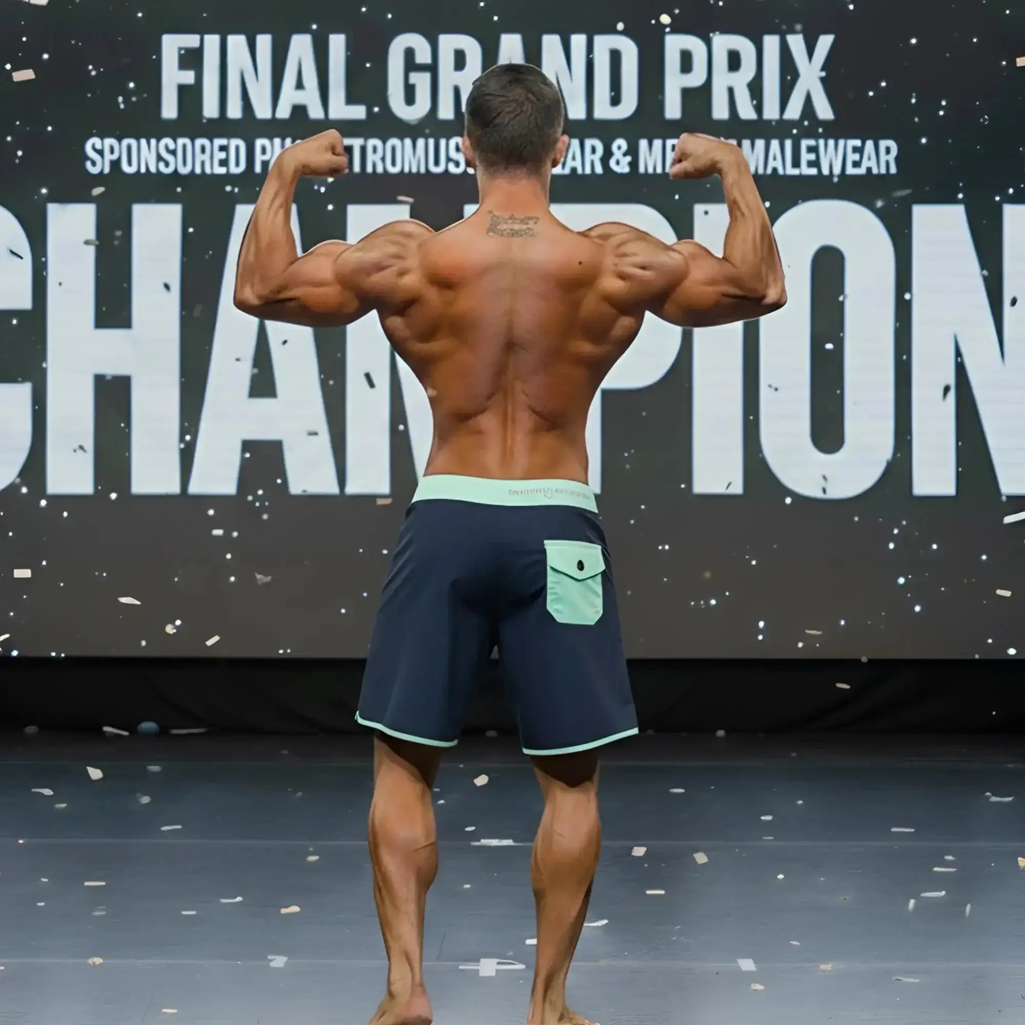 A muscular man wearing MetroMaleWear MetroMuscleWear marine physique board shorts in navy blue.