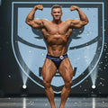 A muscular man flexes in royal blue and black metro musclewear mark competition briefs with number 23 waistband
