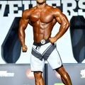 A muscular man wearing metro musclwear metrophysique white board shorts with a logo on the lower right leg