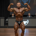 A muscular man flexing in black MetroMaleWear MetroMuscleWear obsidiana competition briefs with white bull logo