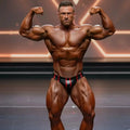 A muscular man flexing in black and red striped metro musclwear competition briefs on stage