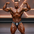 A muscular man wearing metromalewear metromusclewear stripe competition suit white 4974-42 in black and white briefs
