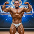 A muscular man wearing MetroMaleWear posingwear snake skin white and gray patterned competition briefs with number 18