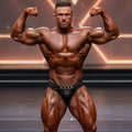 A muscular man wearing metro malewear metromusclewear cadena gold black competition trunks with chain belt