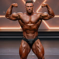 A muscular man wearing MetroMaleWear MetroMuscleWear cadena silver black competition briefs with a silver chain belt