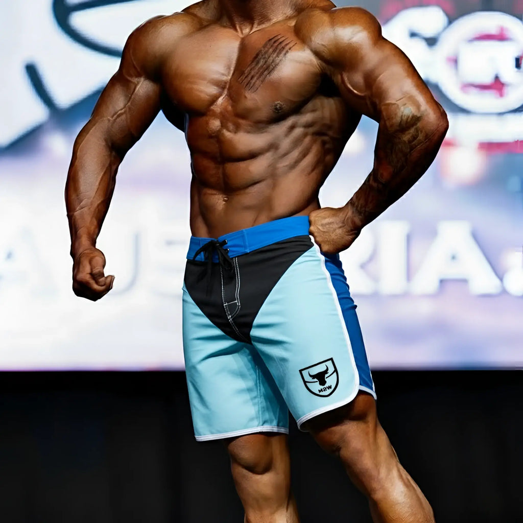 Blue and black MetroMaleWear MetroMuscleWear IFBB Pro men’s physique board shorts with white logo on lower right leg