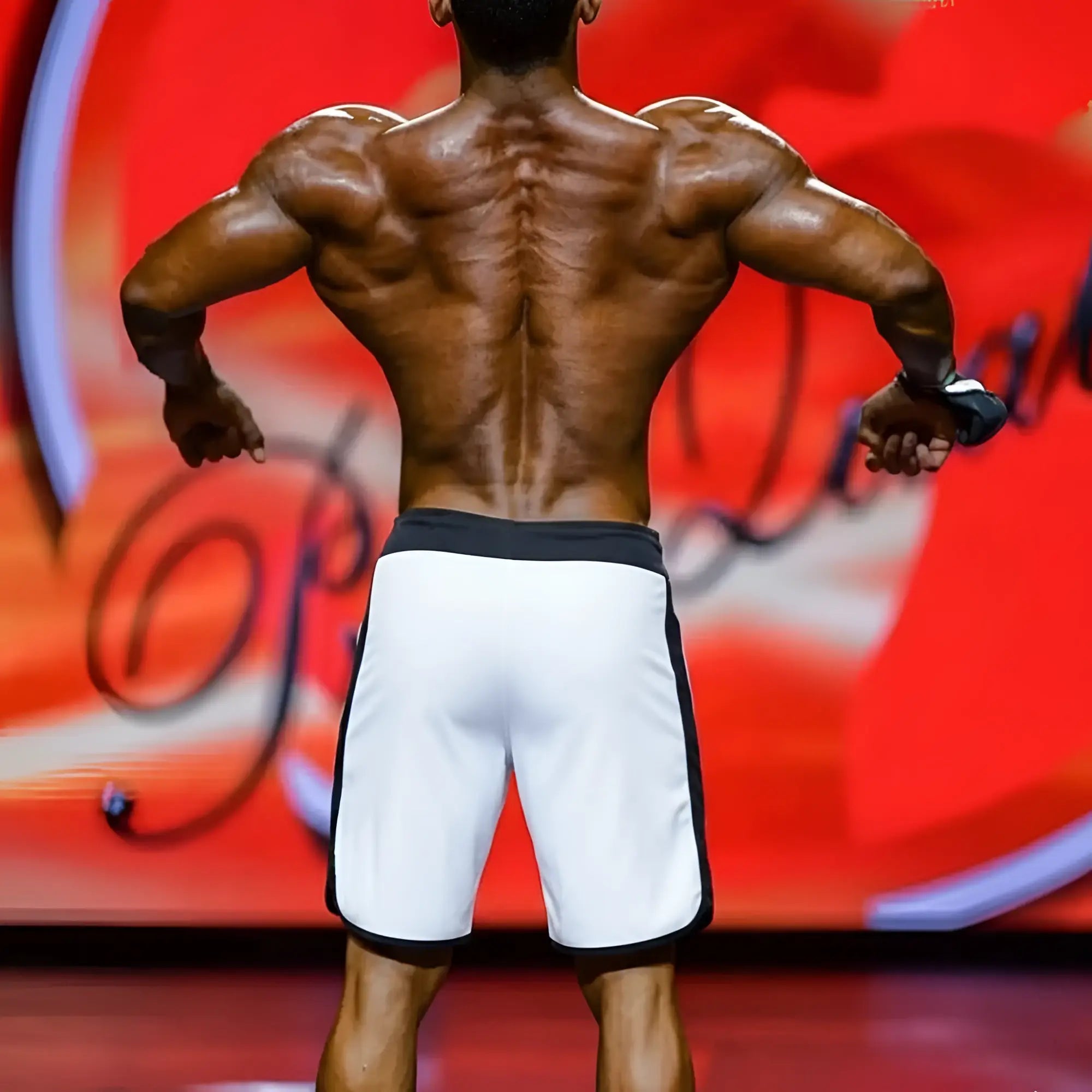 A muscular man showing the back of metroMalewear metromusclewear IFBB pro mens physique board short gradient white with black trim