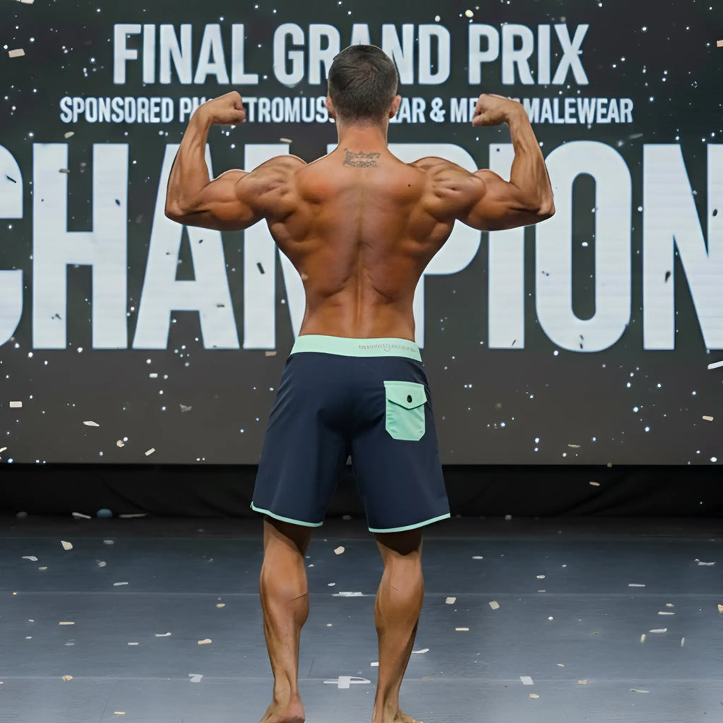 A muscular man wearing MetroMaleWear MetroMuscleWear marine physique board shorts in navy blue with light green waistband and pocket