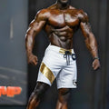 White MetroMaleWear physique board short with gold diagonal stripe, matching belt loop, black drawstring, and logo patch
