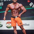 Orange athletic shorts with black waistband and drawstring featuring a small shield logo on the lower right leg