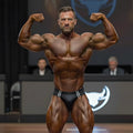 A muscular man flexing in black MetroMaleWear versatile leather swim briefs with white stripes on stage competition
