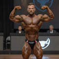 A muscular man wearing metroMalewear versatile swim brief leather II in black red and white stripes at a bodybuilding contest