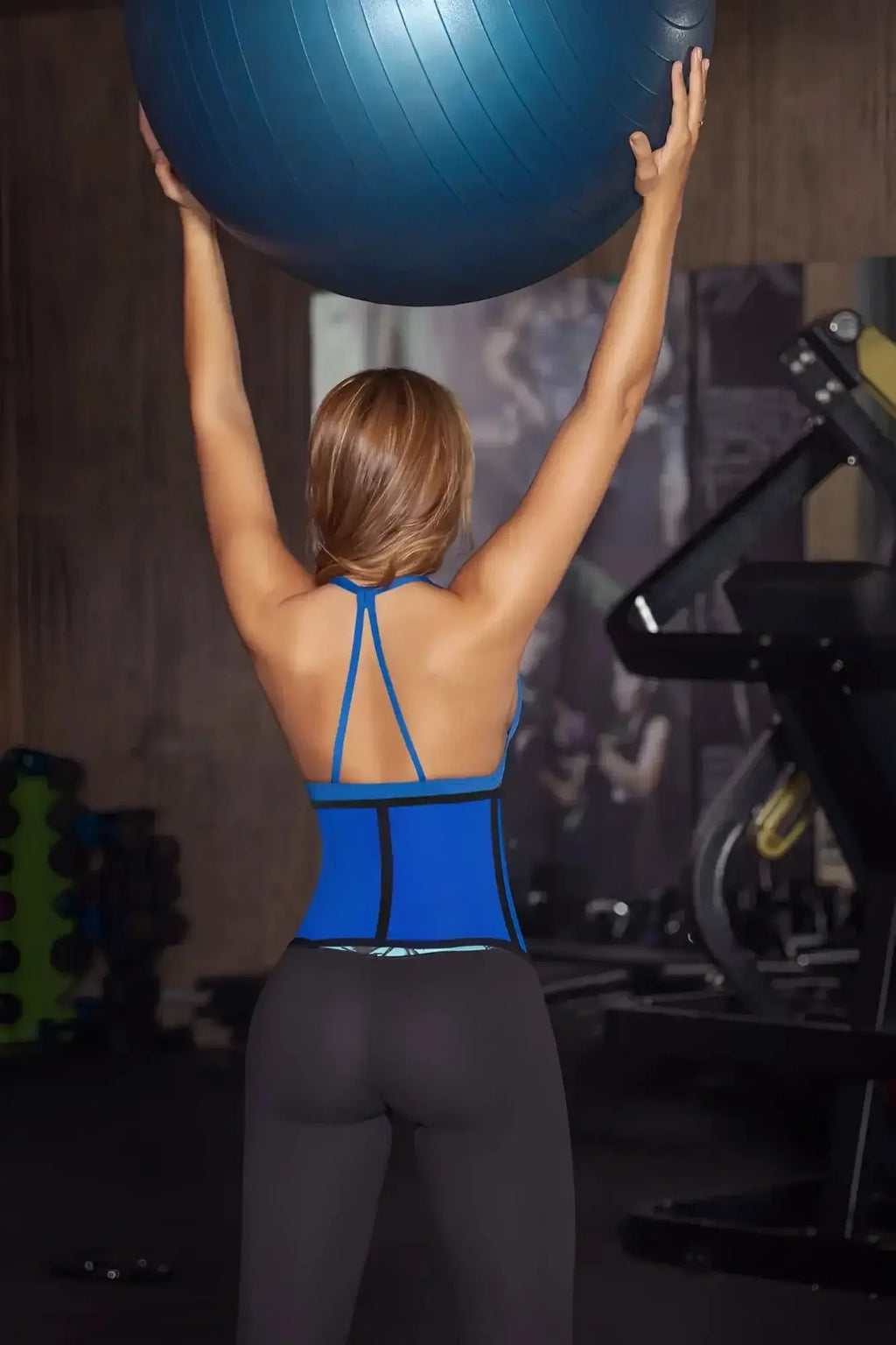 A woman holding a blue moldeate 8031 workout waist cincher exercise ball in a gym setting