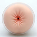 A peach-colored silicone anal plug with a black opening and radial indentations in clear plastic for Naked Factory Anna