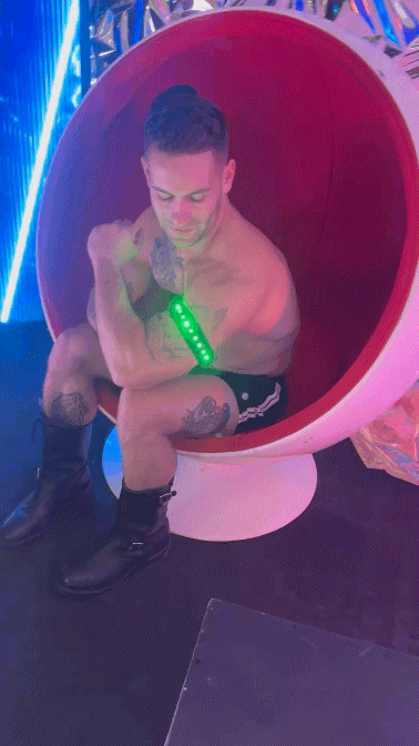 A man sits in a futuristic red and white spherical chair with glowing blue neon lights in the prismaglow armband setting