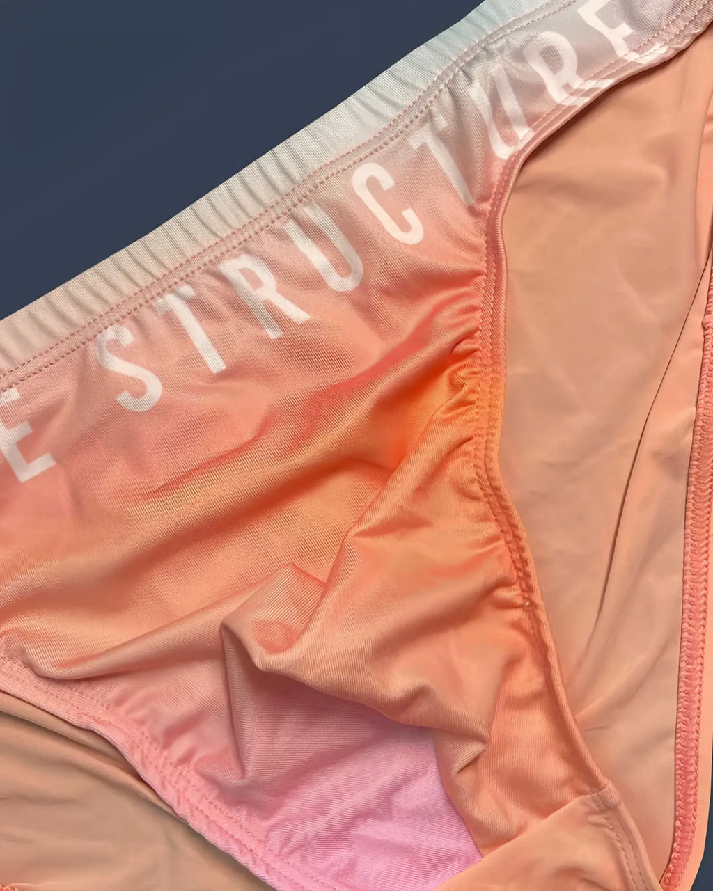 Peach and pink gradient fabric bikini bottom with structure printed in white on the waistband in orange color