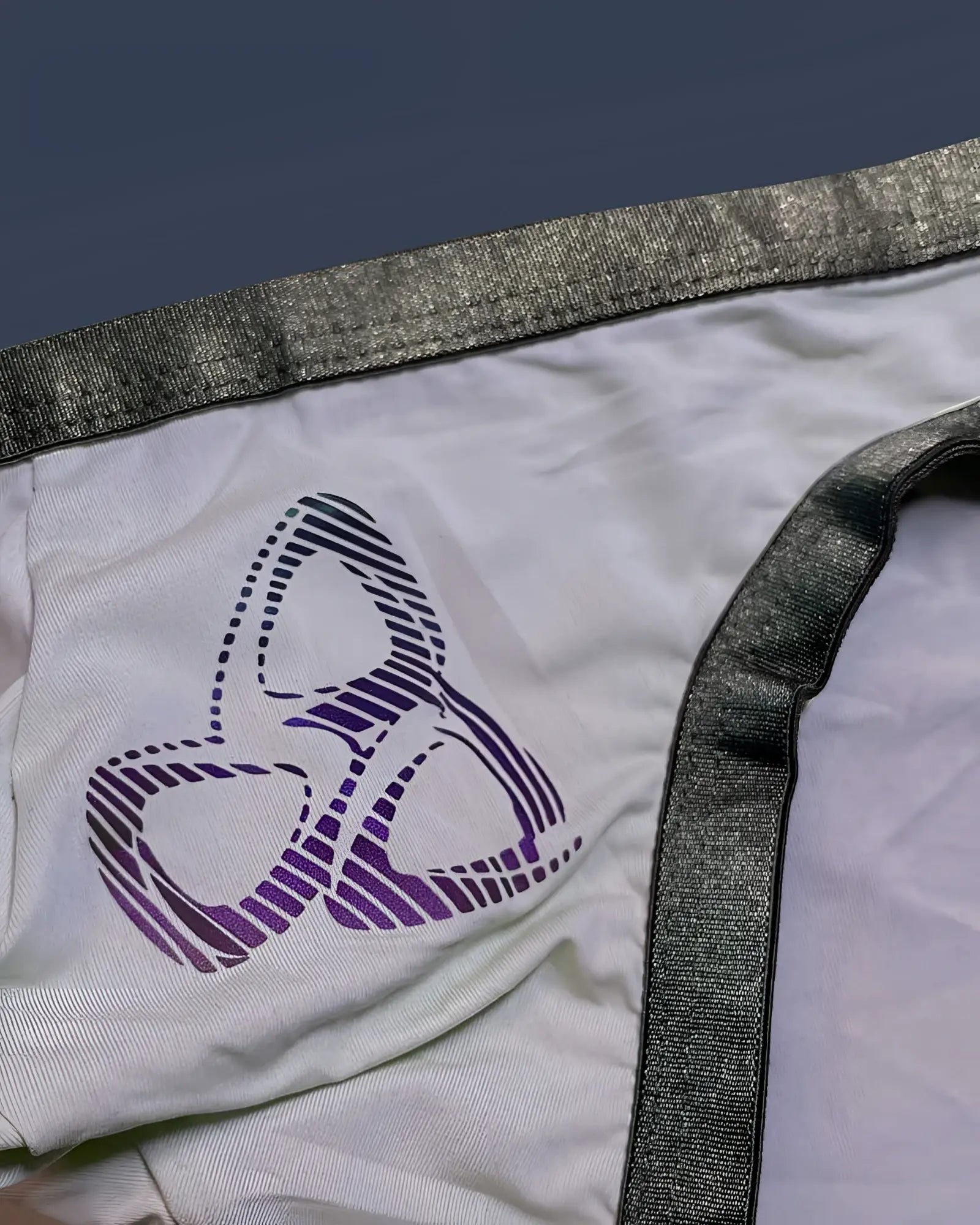 White fabric bare bikini underwear by private structure with a purple and black striped logo and shiny gray waistband trim