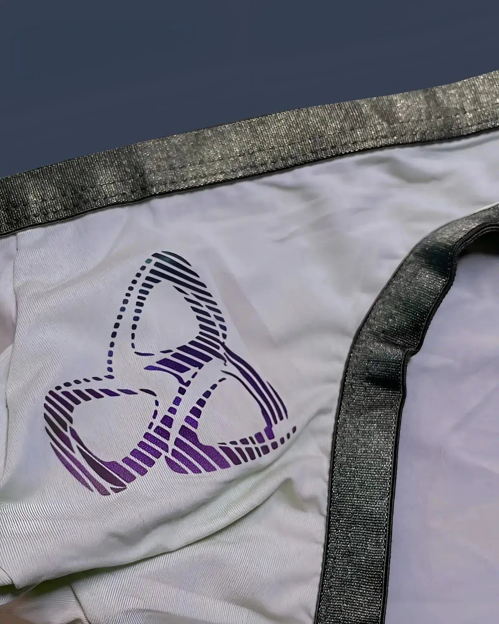White fabric bare bikini underwear by private structure with a purple and black striped logo and shiny gray waistband trim