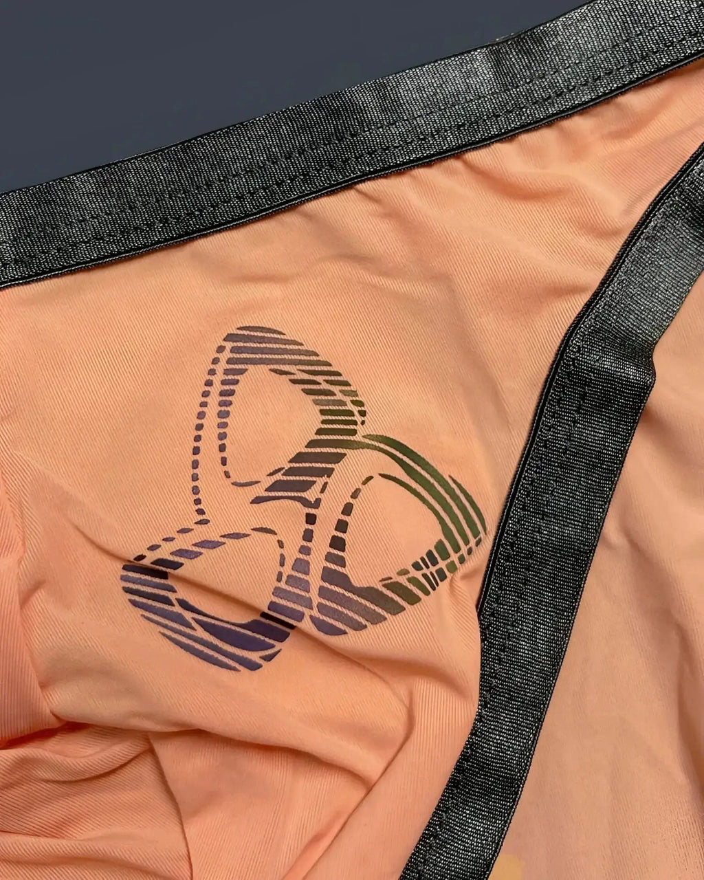 Peach-colored fabric thong with black elastic trim and gradient-striped logo from private structure bare bikini orange