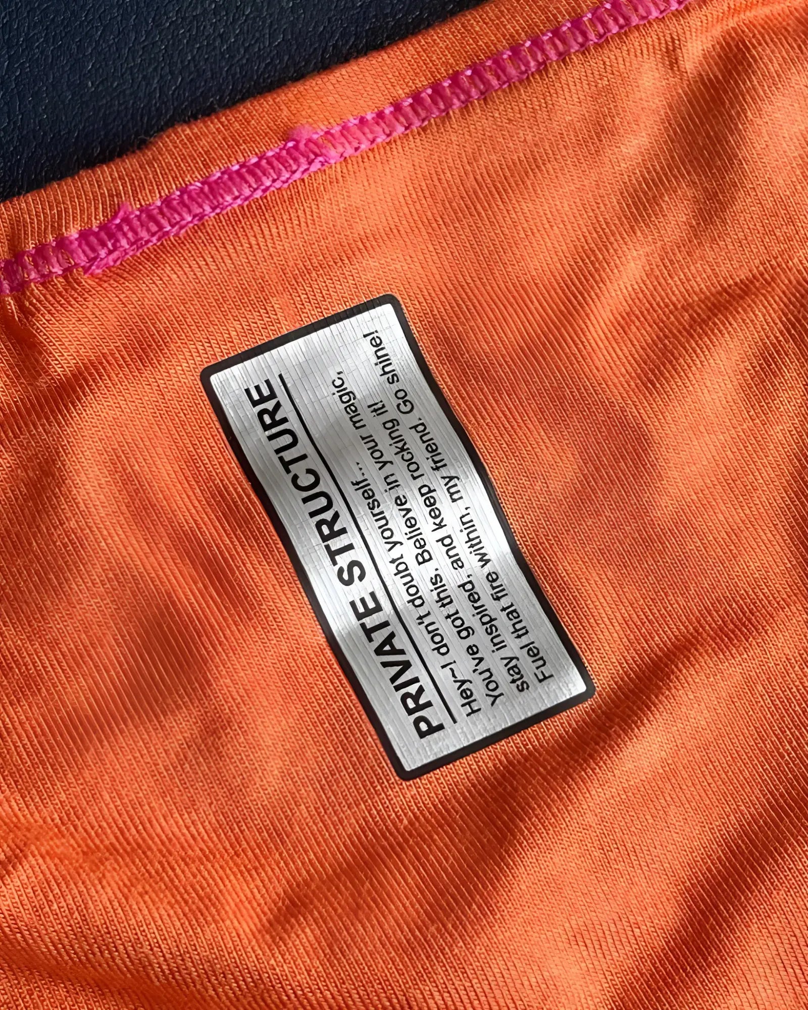 Orange private structure prime eutopia bikini brief with black and silver label stitched along the seam