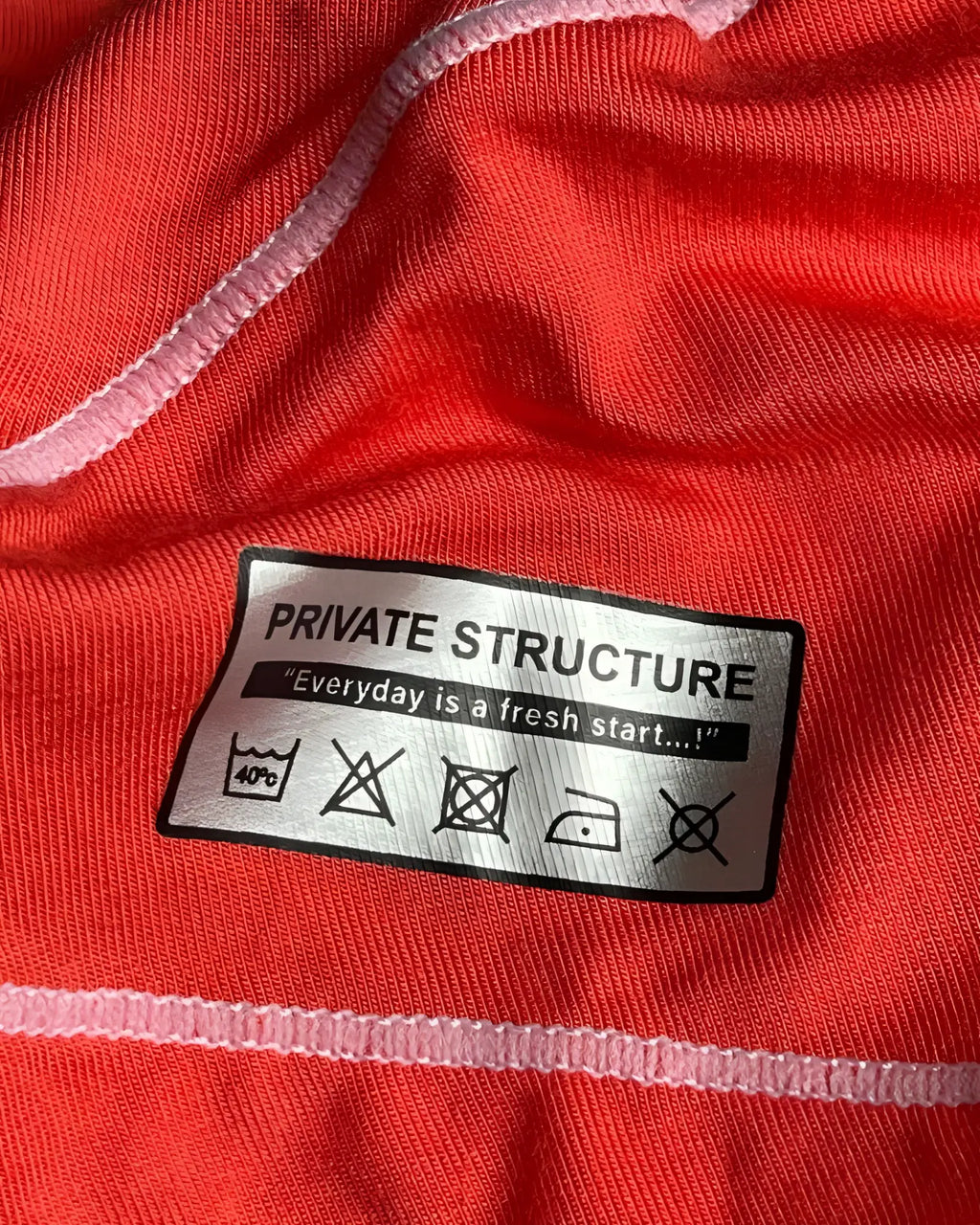A silver rectangular care label with black text reading private structure and laundry instructions on the back of a red hipster brief