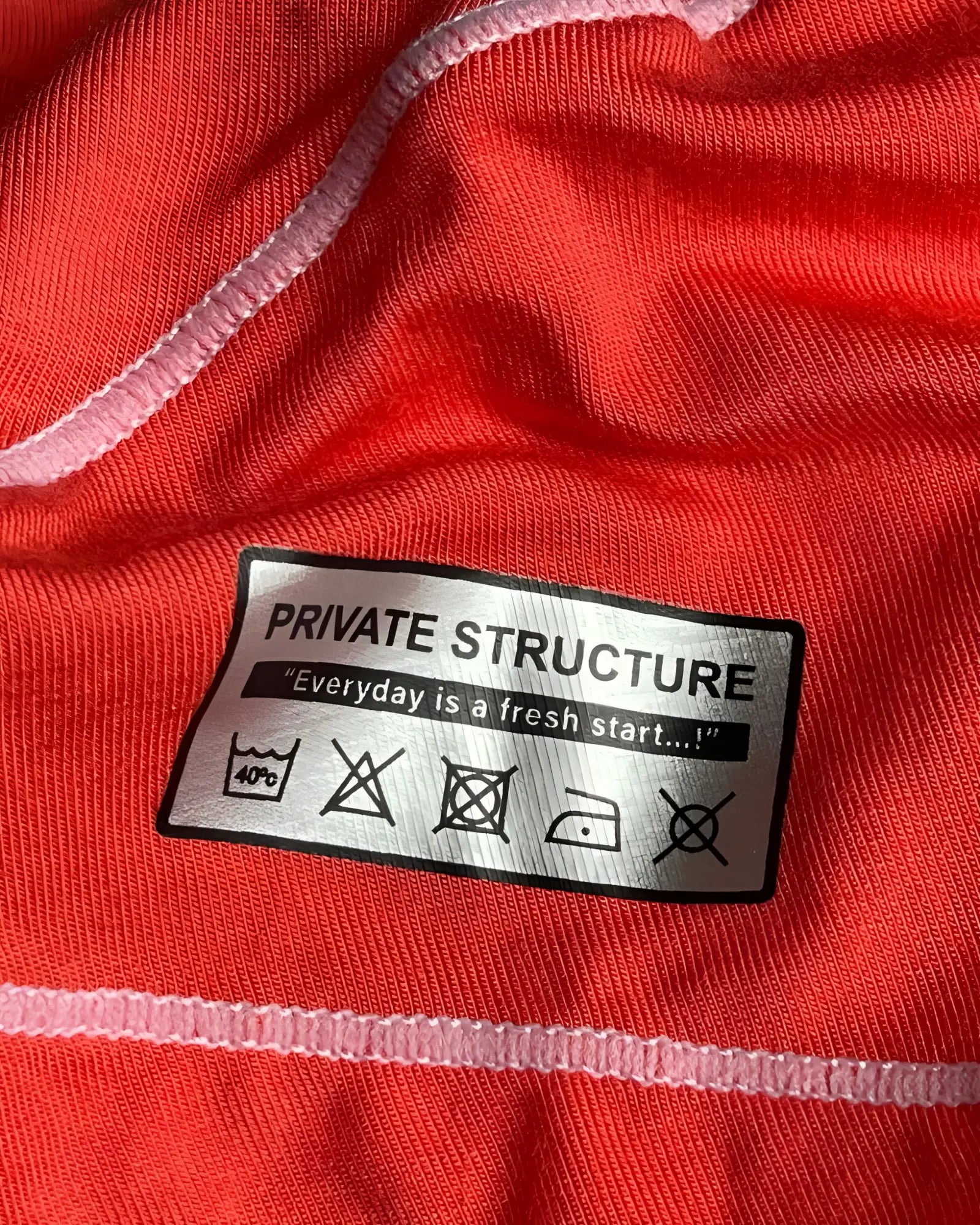 A silver rectangular care label with black text reading private structure and laundry instructions on the back of a red hipster brief