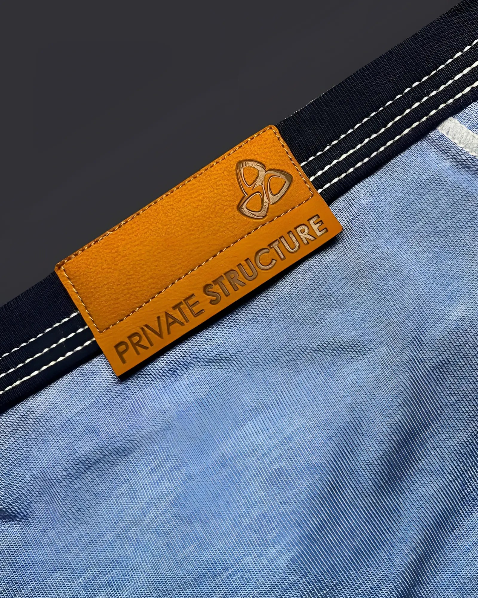 Orange leather brand tag with embossed logo and private structure text on blue denim fabric of mini brief