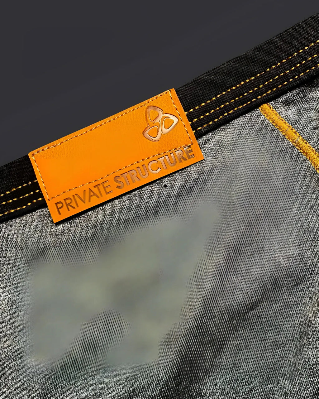 Orange leather brand tag with embossed private structure logo stitched on dark gray denim of barn boy mini brief