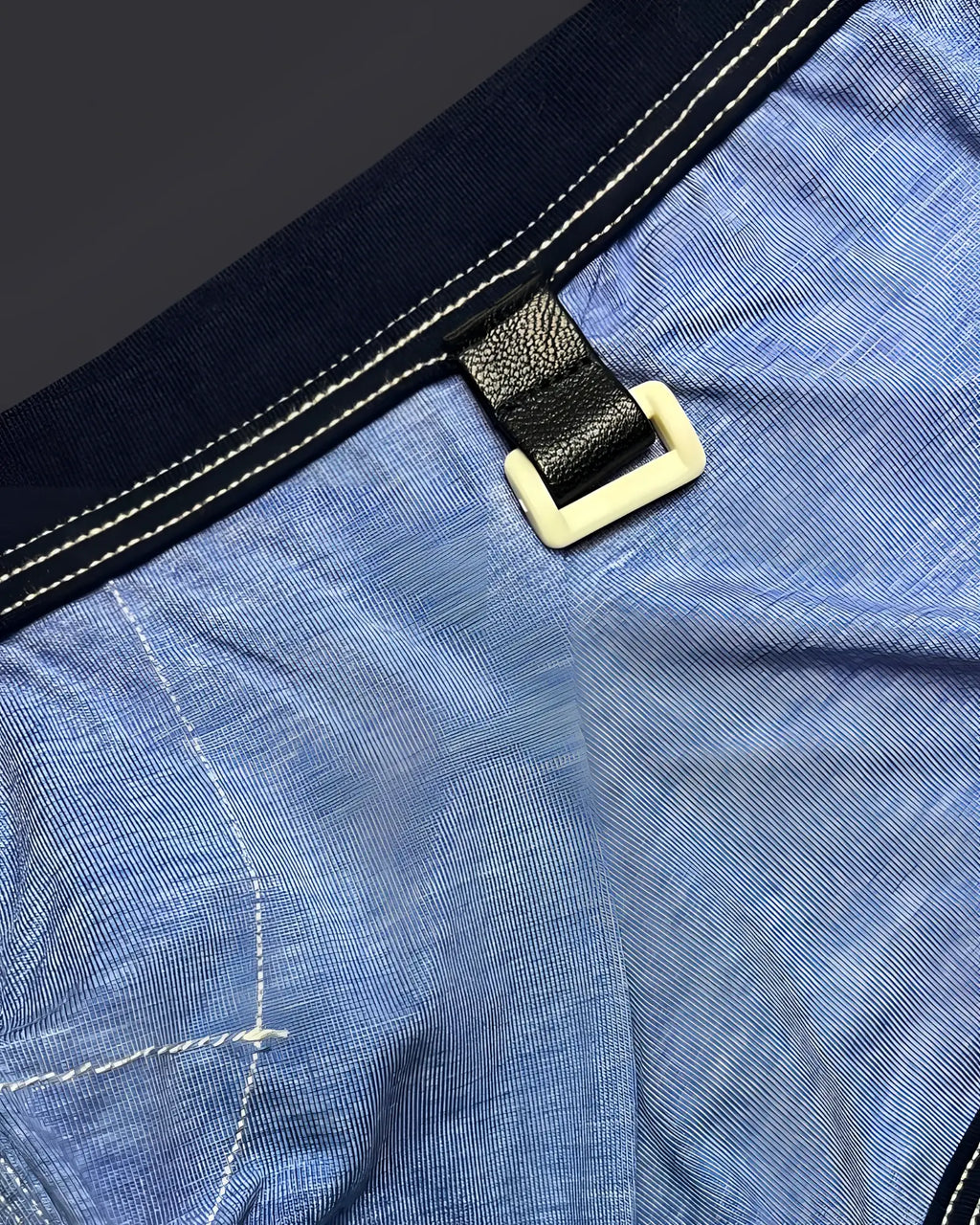 Black leather strap with cream plastic buckle attached to blue denim on private structure barn boy low rise trunk