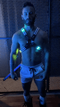 The man is wearing a black and blue rave cross harness with led-lit glowing green lights