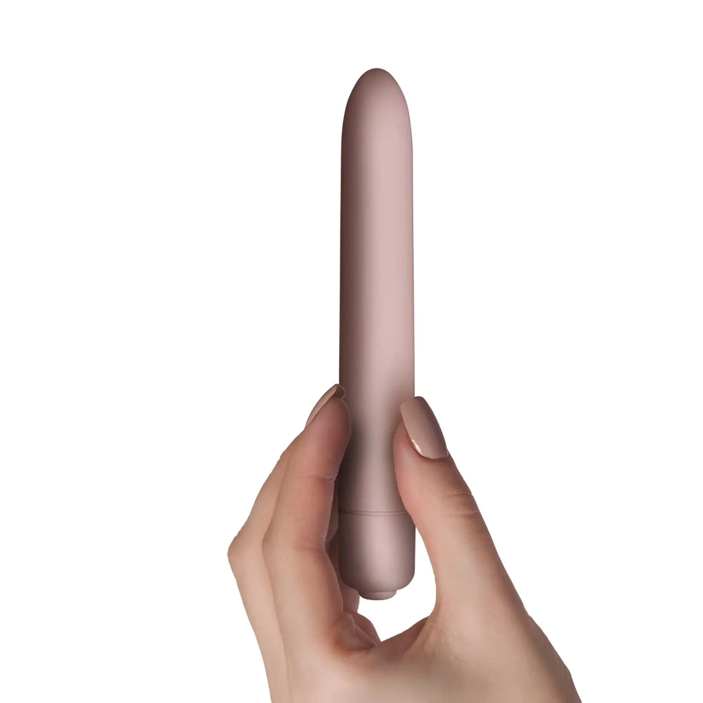 A sleek matte rose gold silicone vibrato wand held gently in a hand rocks off sugarboo bullet vibe blush