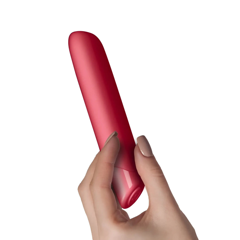 A sleek matte red cylindrical vibrator held gently in a hand rocks off sugarboo cool coral bullet vibe