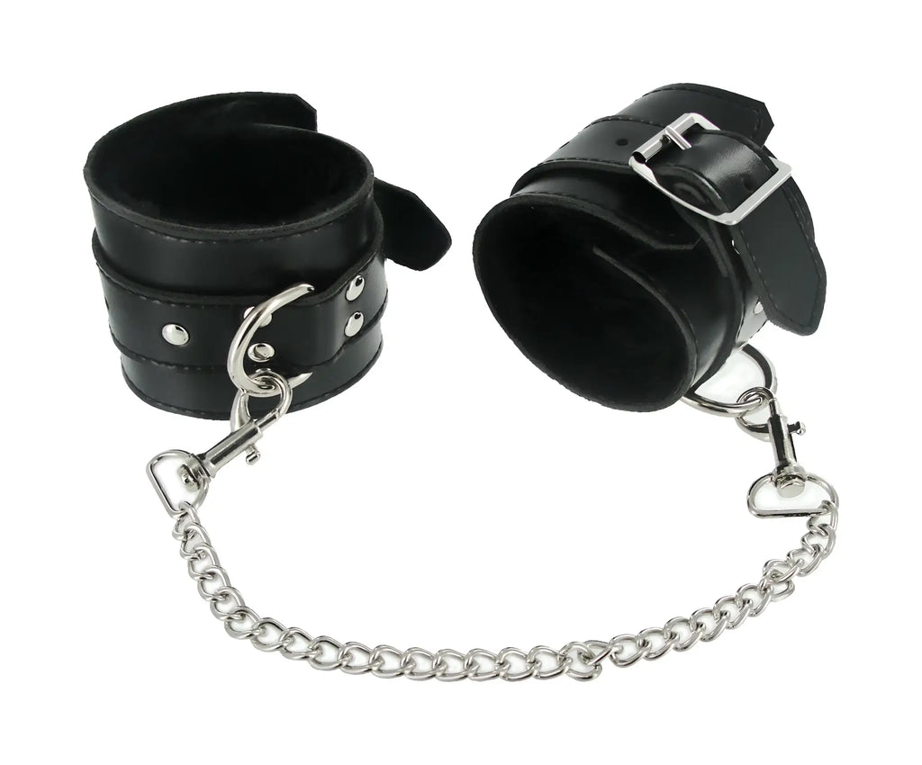 Black leather wrist cuffs with silver metal buckles and chain from the strict 7 pc bondage adventure set