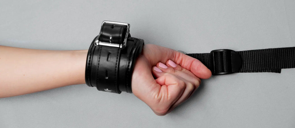 Black leather wrist restraint from strict bed restraint kit with silver-toned buckle and adjustable strap