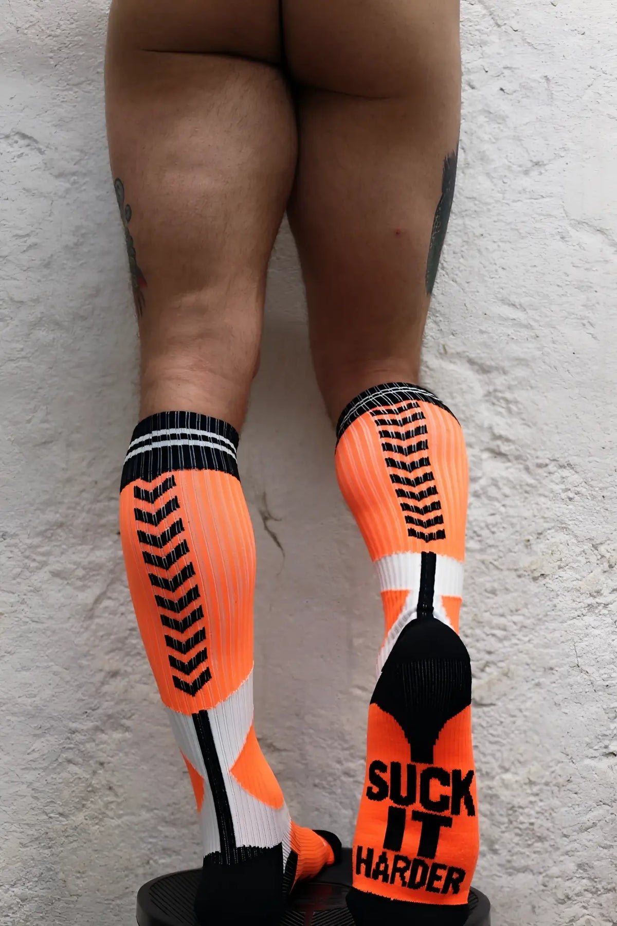 Bright orange sucker socks with black and white accents featuring bold suck it harder graphic on the foot
