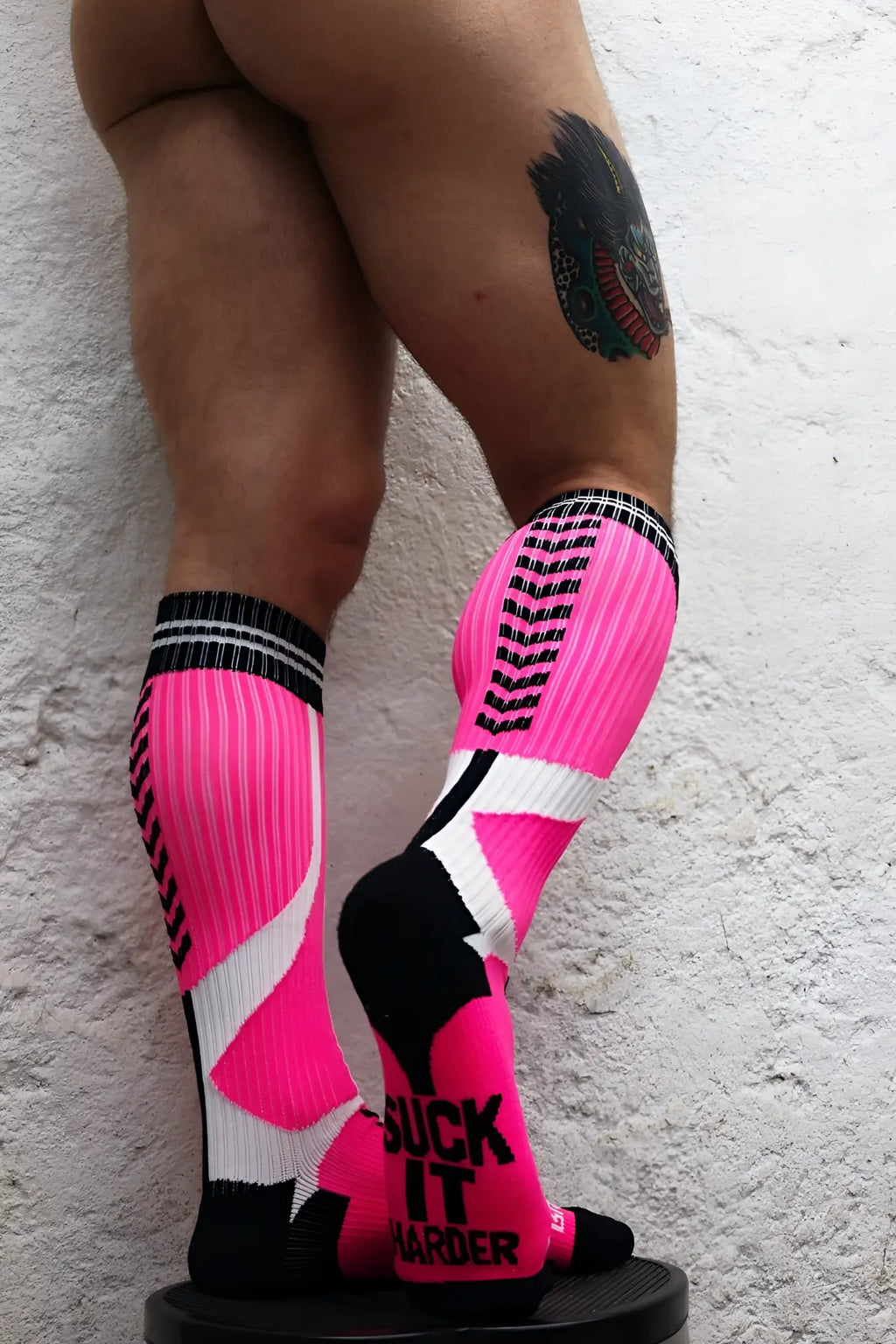Vibrant pink white and black athletic compression sucker socks with bold geometric patterns and suck it harder text on foot