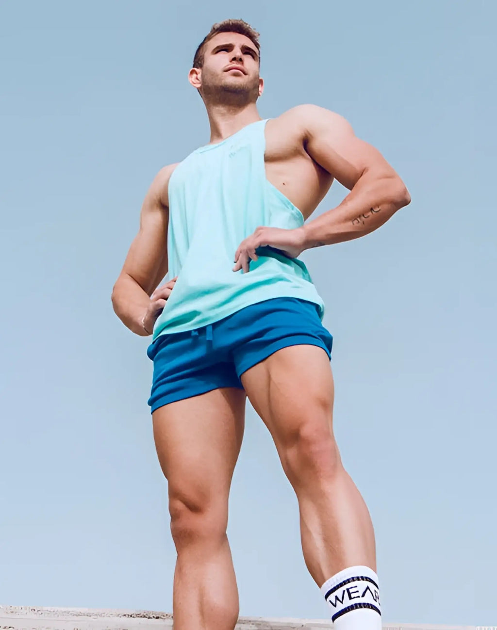A muscular man wearing supawear 4 inch jersey shorts and a sleeveless tank top in lapis blue