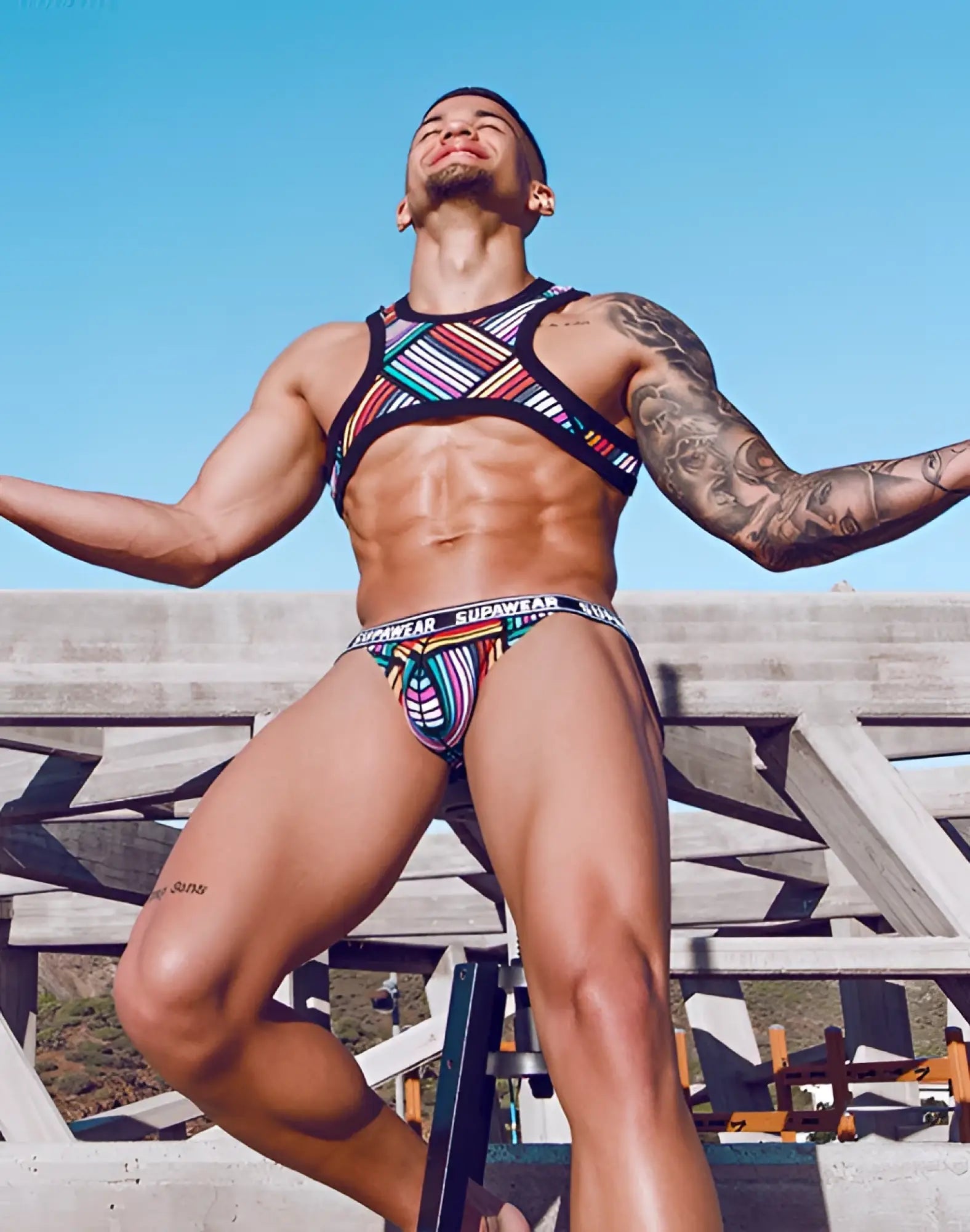 Colorful striped supawear swim trunks with black trim and matching sports bra in supawear pow pride rainbow design