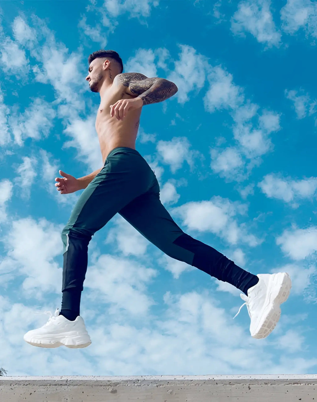 A man in mid-air wearing supawear pro-training pants in boost green with black panels and white chunky sneakers
