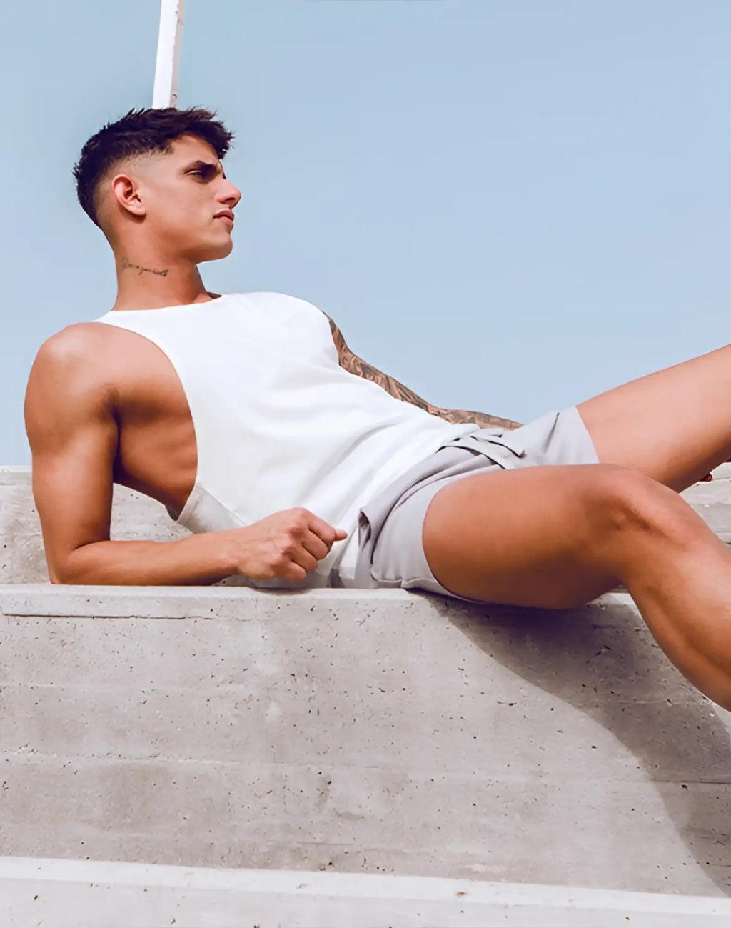 A man wearing a supawear grey white racer back singlet with a sleeveless tank top design and light gray shorts