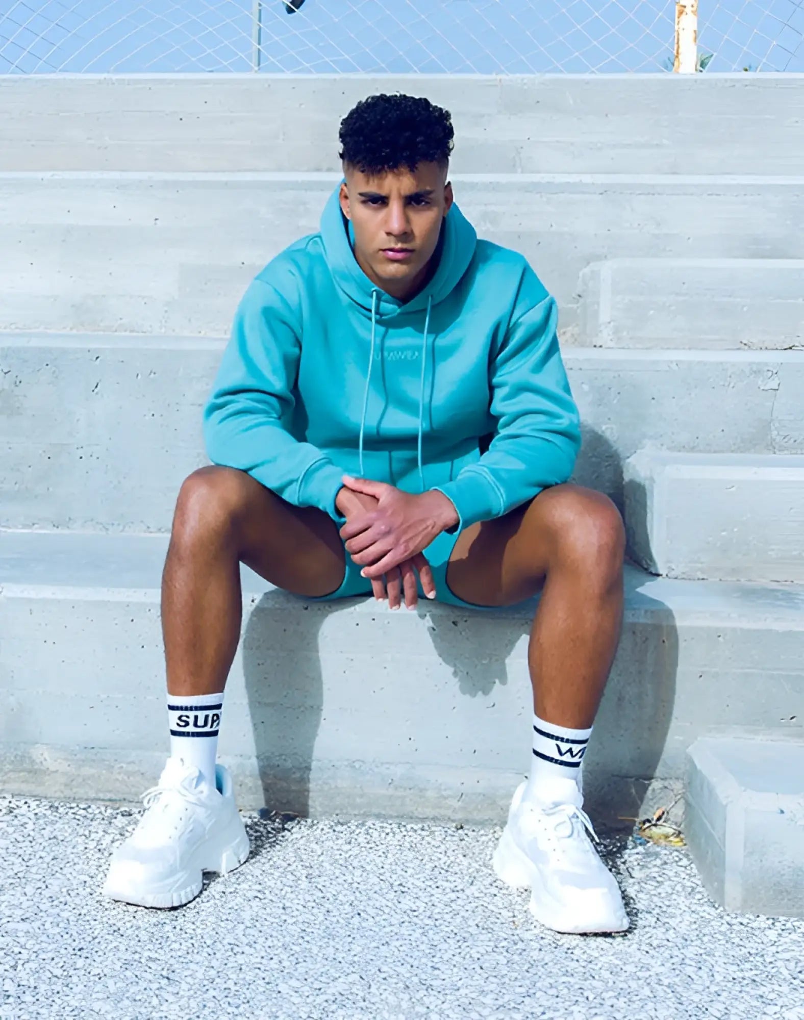 A man wearing a SUPAWEAR recovery hoodie in reboot green with matching shorts and white chunky sneakers